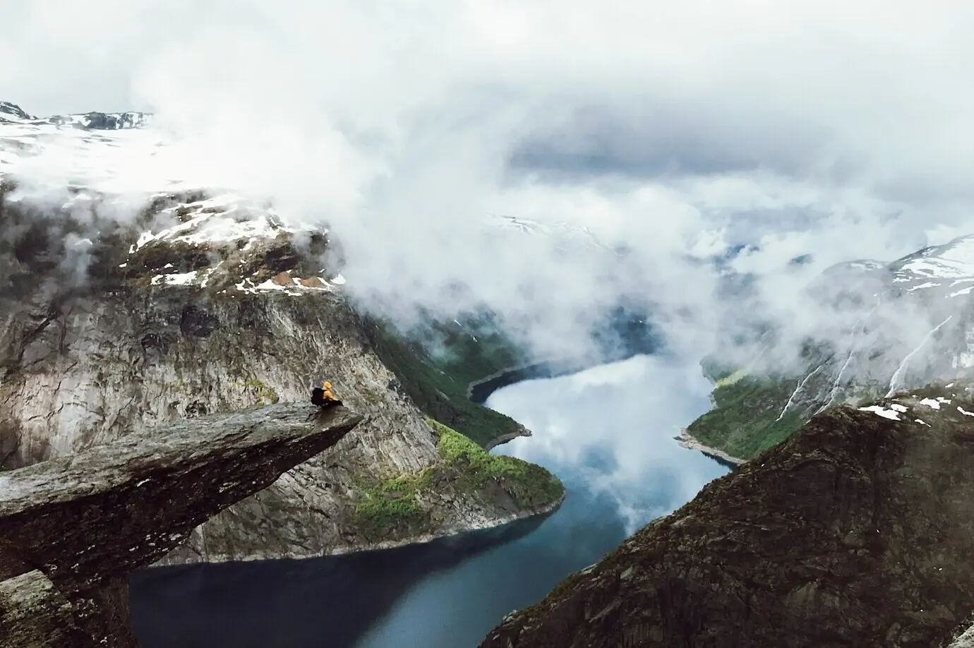 Un hombre está sentado en el extremo de Trolltunga, frente a las montañas.